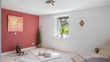 A room with a red accent wall, a window with a view of greenery, a white sofa, and a floor lamp.