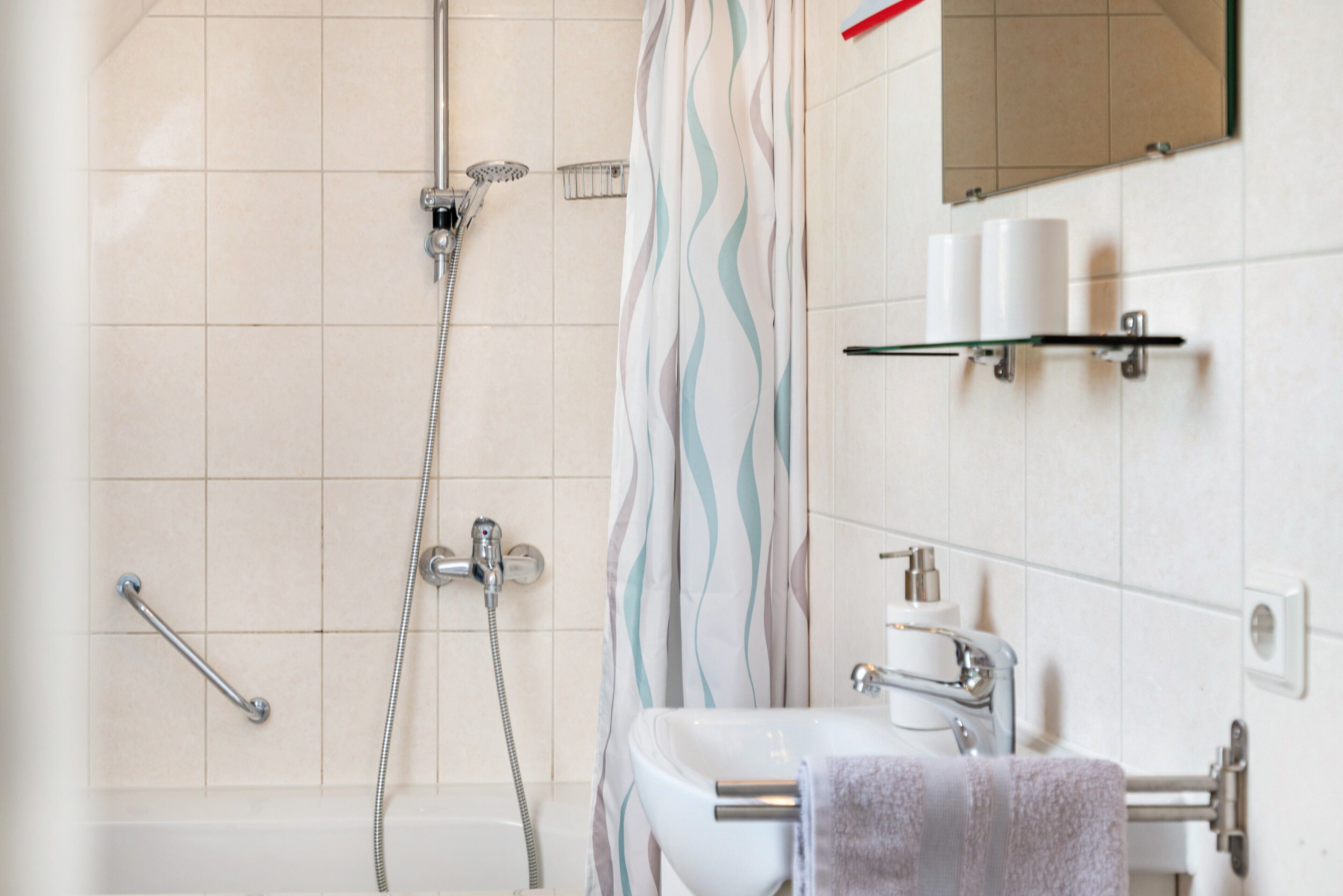 Un baño con ducha, lavabo, espejo y toallero.