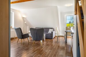 A modern living room with a sofa, two armchairs, a coffee table, and a kitchen area with a window. - Sunrise Holiday Apartment – Your Retreat in the Heart of Nature (Herzberg am Harz)