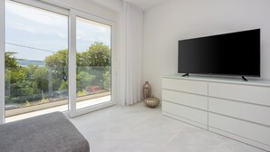 Ein modernes Zimmer mit großem Fenster, einem Flachbildfernseher, einem weißen Schrank und einem grauen Sofa.