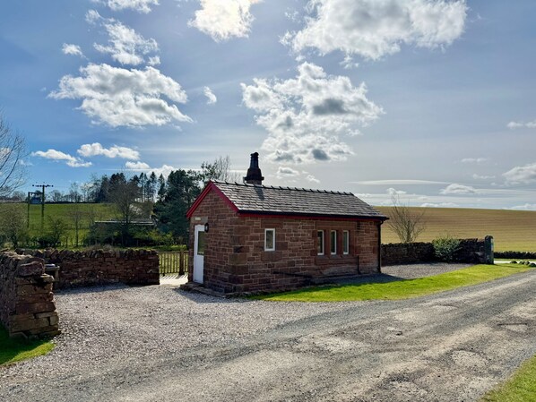 A small stone building with a red roof, a chimney, and a gravel driveway.
