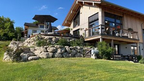 Una casa moderna de dos pisos con un muro de contención de piedra, un balcón y un patio.