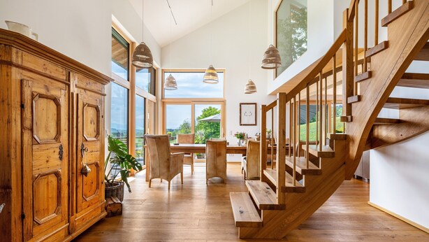 Una habitación amplia con una escalera de madera, ventanas grandes y un comedor.