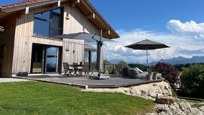 Una casa moderna de madera con terraza, mobiliario exterior y vistas a la montaña.