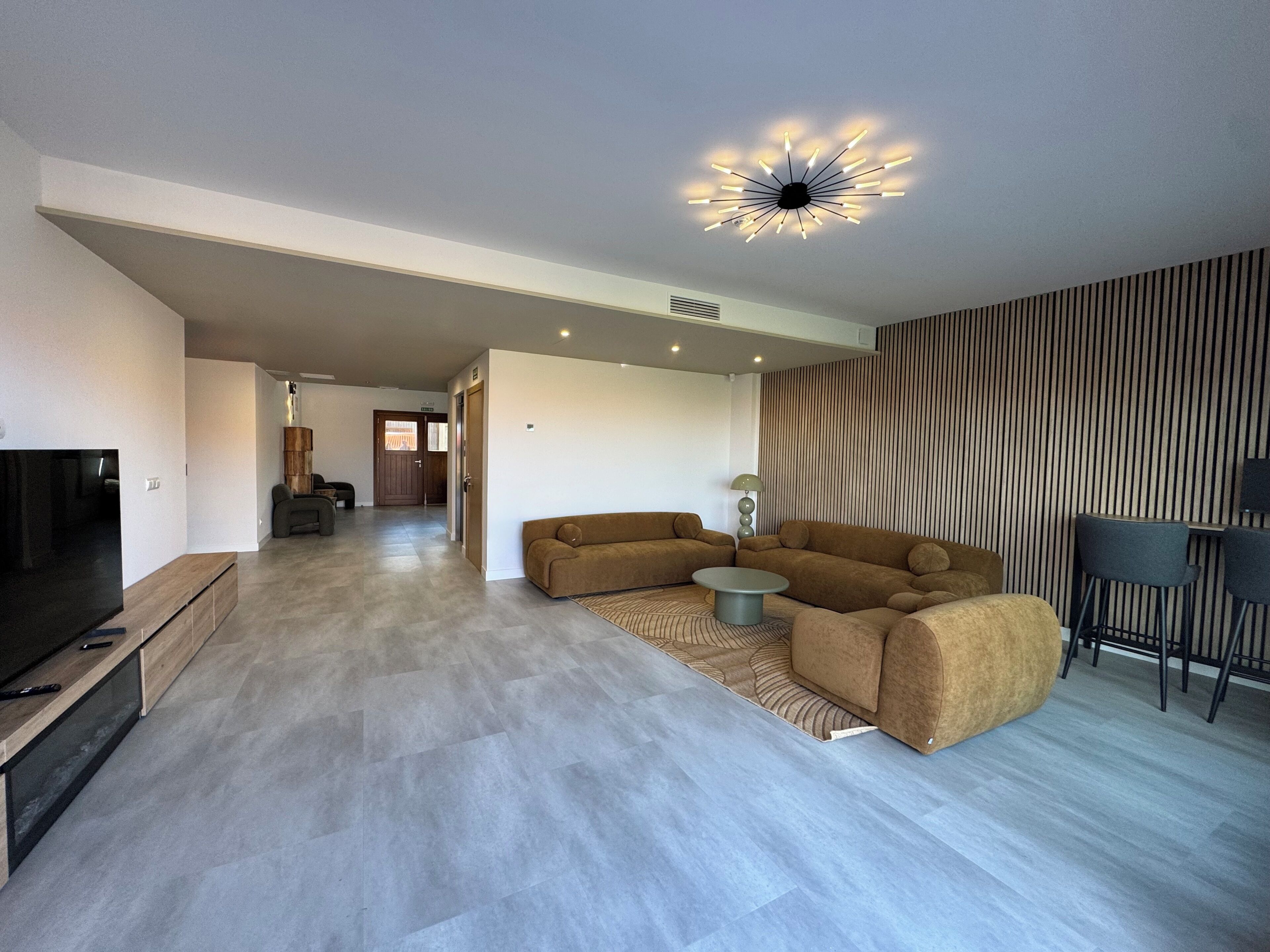 Una sala de estar moderna con televisor de pantalla plana, un sofá modular, una mesa de centro y una lámpara de techo original.