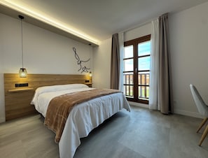 Ein modernes Schlafzimmer mit einem Holz-Kopfteil, einem großen Bett mit weißer und brauner Bettwäsche, einem Nachttisch mit Lampe, einem Fenster mit Vorhängen und Blick ins Freie.