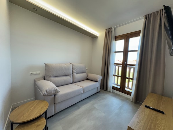 A modern living room with a sofa, a small wooden table, and a TV mounted on the wall.