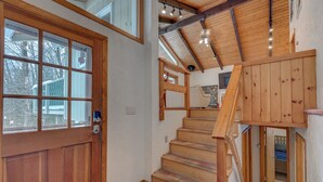 Eine Holztreppe mit Blick auf ein Schlafzimmer, eine Tür mit Glasscheiben und eine Steinsäule.