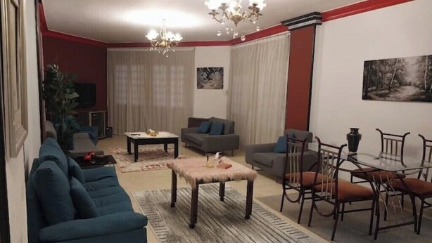 A living room with a sofa, a coffee table, a dining table with chairs, a chandelier, and a painting on the wall. -  Entire rental, Perfect Abbass el akkad flat with balcony (cairo)