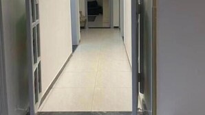 Un couloir étroit au sol carrelé, une porte au fond et un petit marchepied menant à un espace aux couleurs sombres.