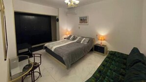 Une chambre à coucher avec un lit, des lampes de chevet, une télévision, une chaise et un canapé.