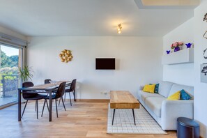Ein modernes Wohnzimmer mit Essbereich, einer Couch, einem an der Wand montierten Fernseher und einem großen Fenster.