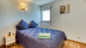 A bedroom with a bed, nightstand, wall-mounted lamp, window, and a painting. - Cosy Renovated Apartment Near the Beach With Balcony (Lattes)
