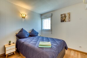 Ein Schlafzimmer mit Bett, Nachttisch, Wandlampe, Fenster und einem Gemälde.