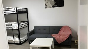 Ein Zimmer mit einem Etagenbett, einem grauen Sofa, einem weißen Couchtisch und einer rosa Decke.