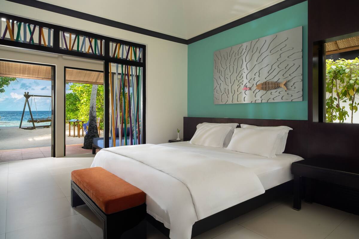 Un dormitorio con cama, un banco, vista al océano y una obra de arte en la pared.