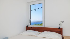 Un lit avec une literie blanche, une tête de lit en bois, une fenêtre donnant sur la mer et une table de chevet avec une lampe.