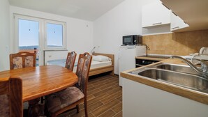 Une pièce de taille modeste comprenant un lit, une table à manger avec des chaises, un coin cuisine équipé d’un four à micro-ondes et d’un évier.