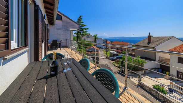 Un balcon avec une table en bois, des chaises et une bouteille de vin.
