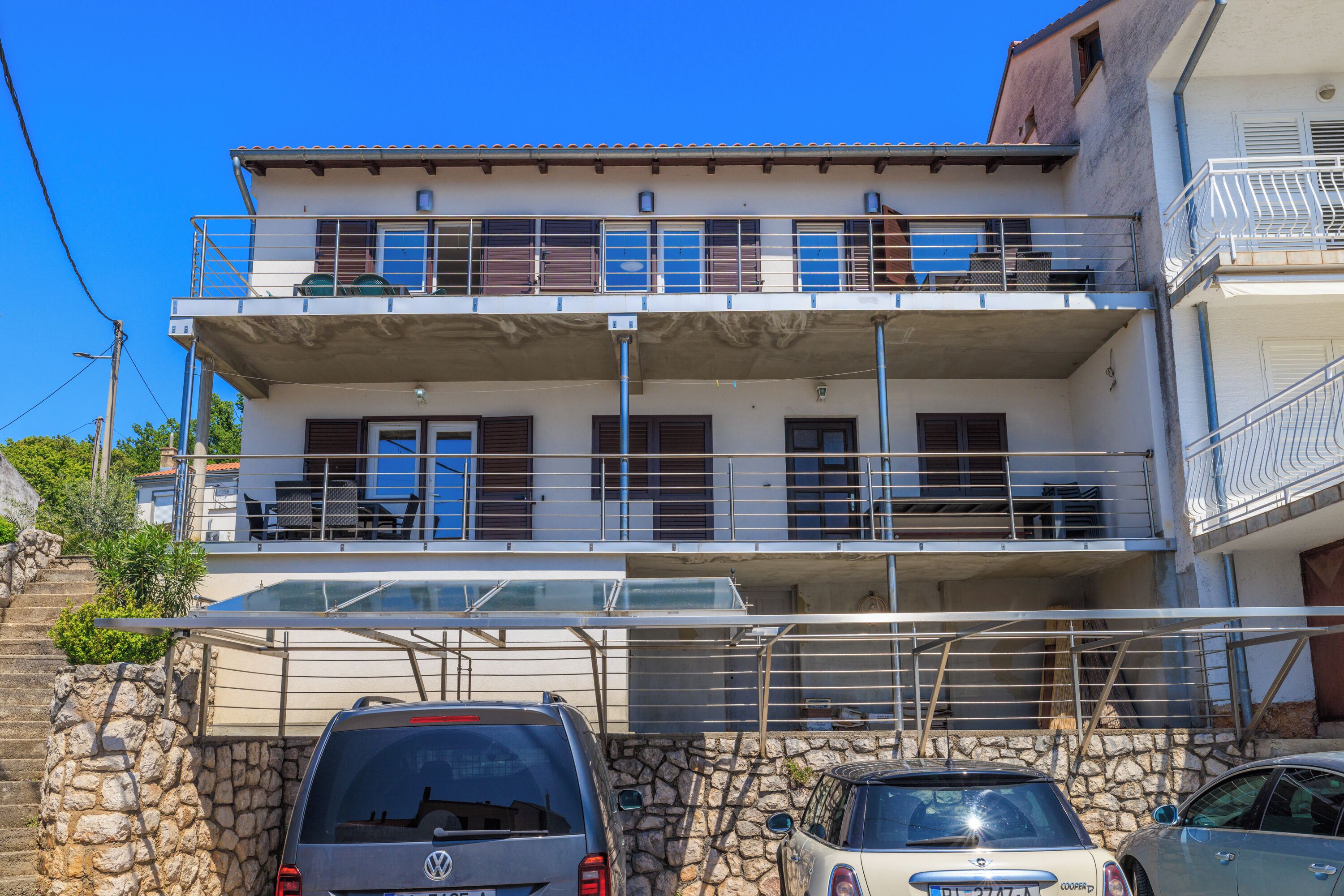 Un immeuble à plusieurs étages, doté de balcons, d’un mur en pierre et de voitures garées.