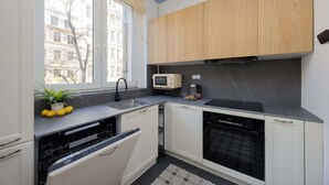 A compact kitchen with a microwave, sink, and oven, a potted plant, and a window with a view of buildings. - Sunny Apartment in the Center | Place to Work (Warszawa)