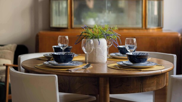 A round dining table with a white vase and blue bowls, set with gold placemats and silverware. - Sunny Apartment in the Center | Place to Work (Warszawa)