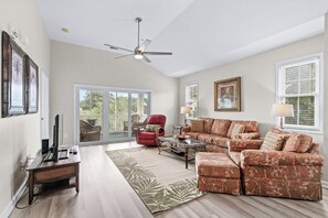 A spacious living room with a ceiling fan, a red armchair, a floral sofa, and a glass coffee table. - 20% off 3-7 nights thru Oct. 2BR 2BA gated community. Near beach. Great getaway! (North Myrtle Beach)