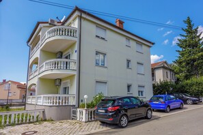 A multi-story residential building with balconies, parked cars, and a clear sky. - Vacation accommodation for 2-4 people - sea view and balcony (Crikvenica)