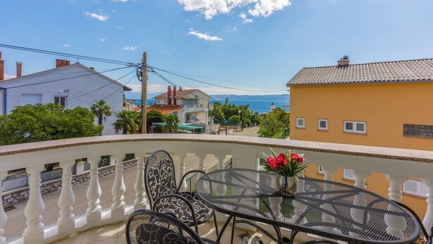Ein Balkon mit Tisch und Stühlen, der auf ein Wohngebiet mit Häusern und Meerblick blickt.