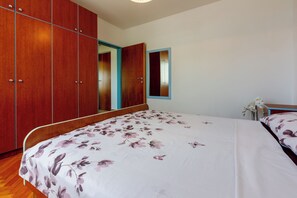 A bedroom with a wooden wardrobe, a bed with floral bedding, and a mirror on the wall. - Vacation accommodation for 2-4 people - sea view and balcony (Crikvenica)