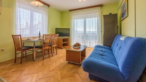 Ein Wohnzimmer mit blauem Sofa, einem Holzesstisch mit Stühlen, einem Fernseher und einem Kühlschrank.