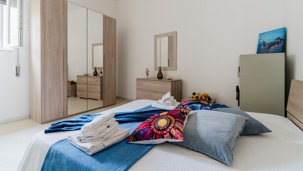Une chambre à coucher avec un lit, une armoire, une commode, un miroir et un tableau accroché au mur.
