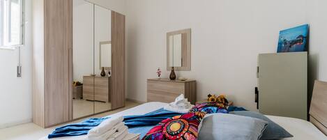 Une chambre à coucher avec un lit, une armoire, une commode, un miroir et un tableau accroché au mur.
