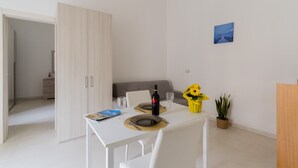 Un coin repas avec une table blanche, deux chaises, une bouteille de vin et un vase rempli de tournesols.