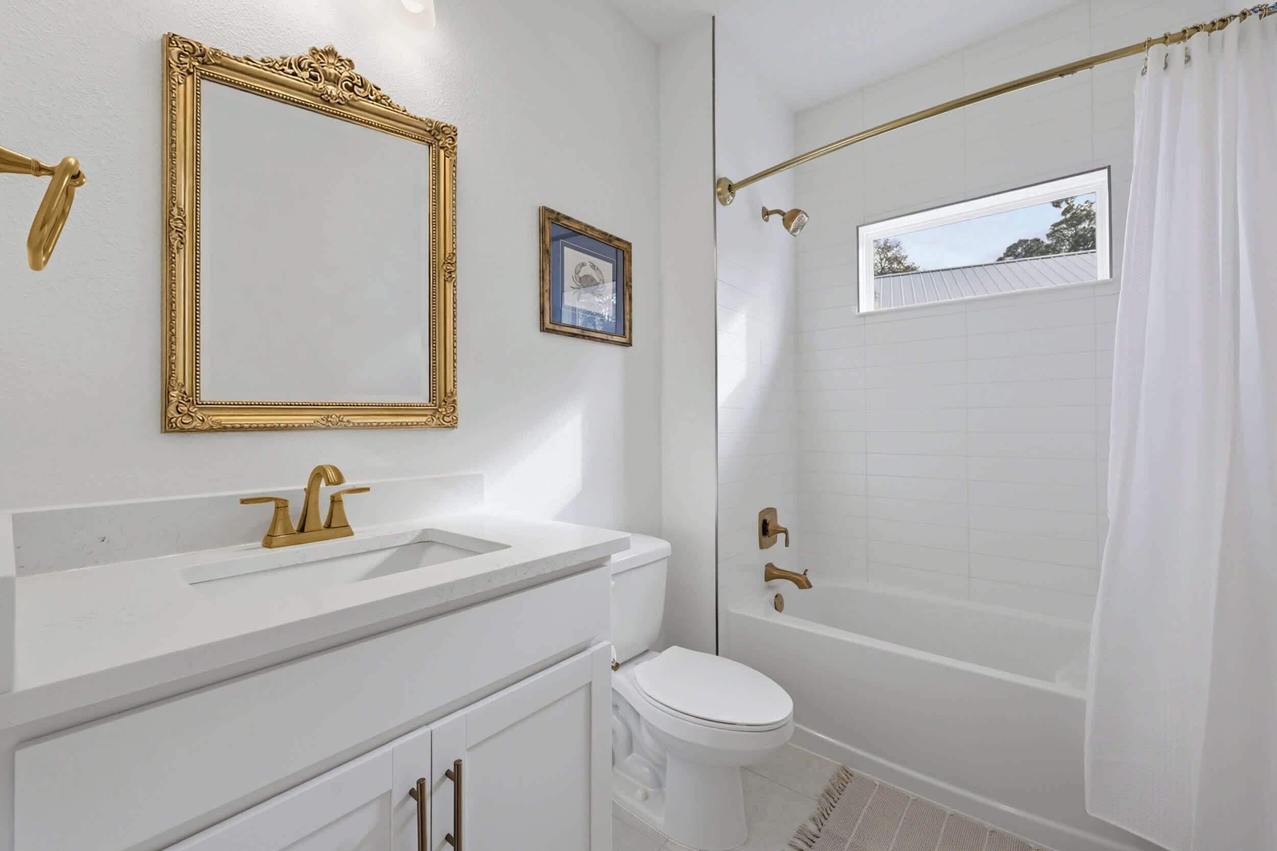 A bathroom with a white sink, gold fixtures, a white toilet, and a shower with a glass door.