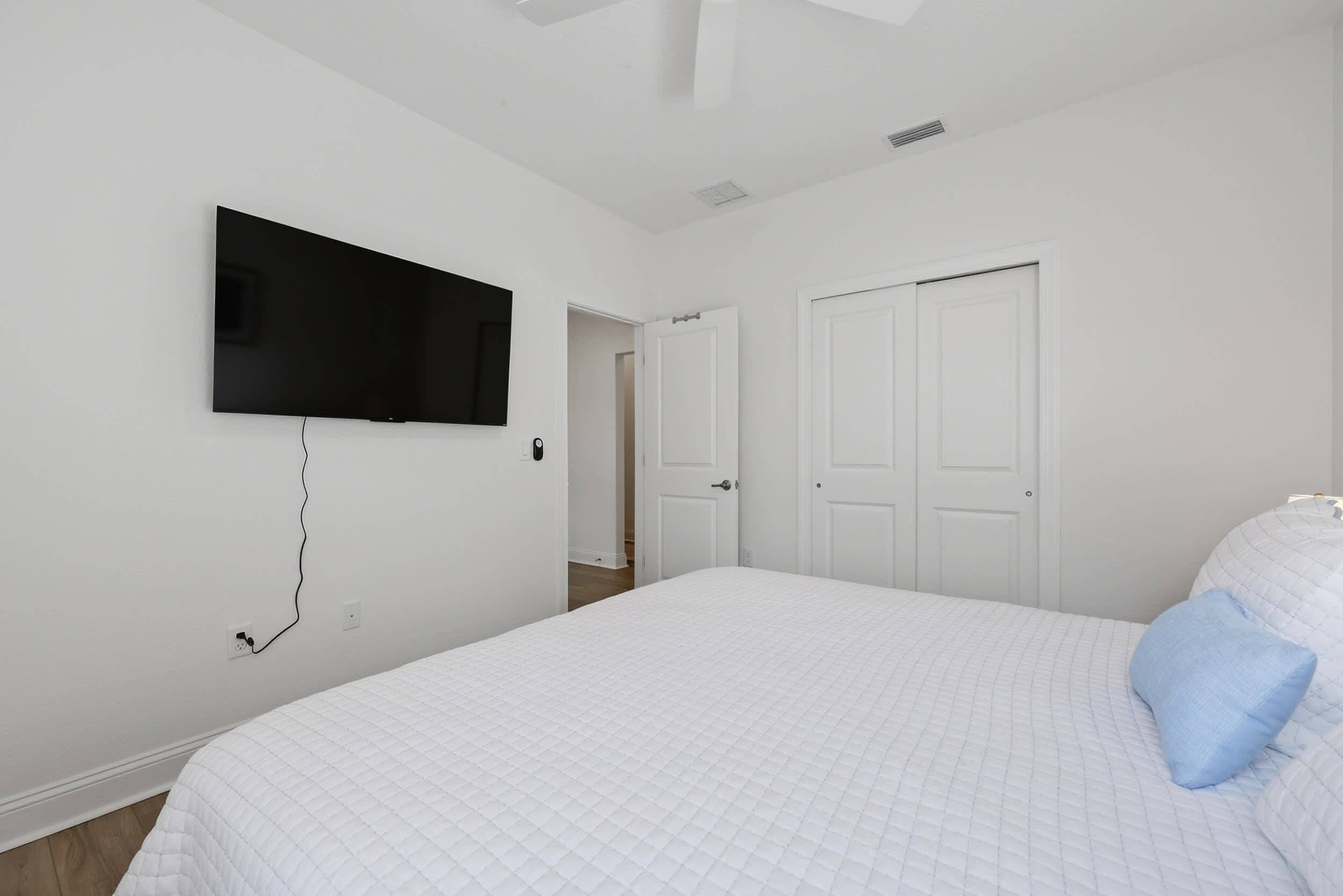 Ein Schlafzimmer mit einem Bett, einem an der Wand befestigten Fernseher und einer Tür zu einem anderen Raum.