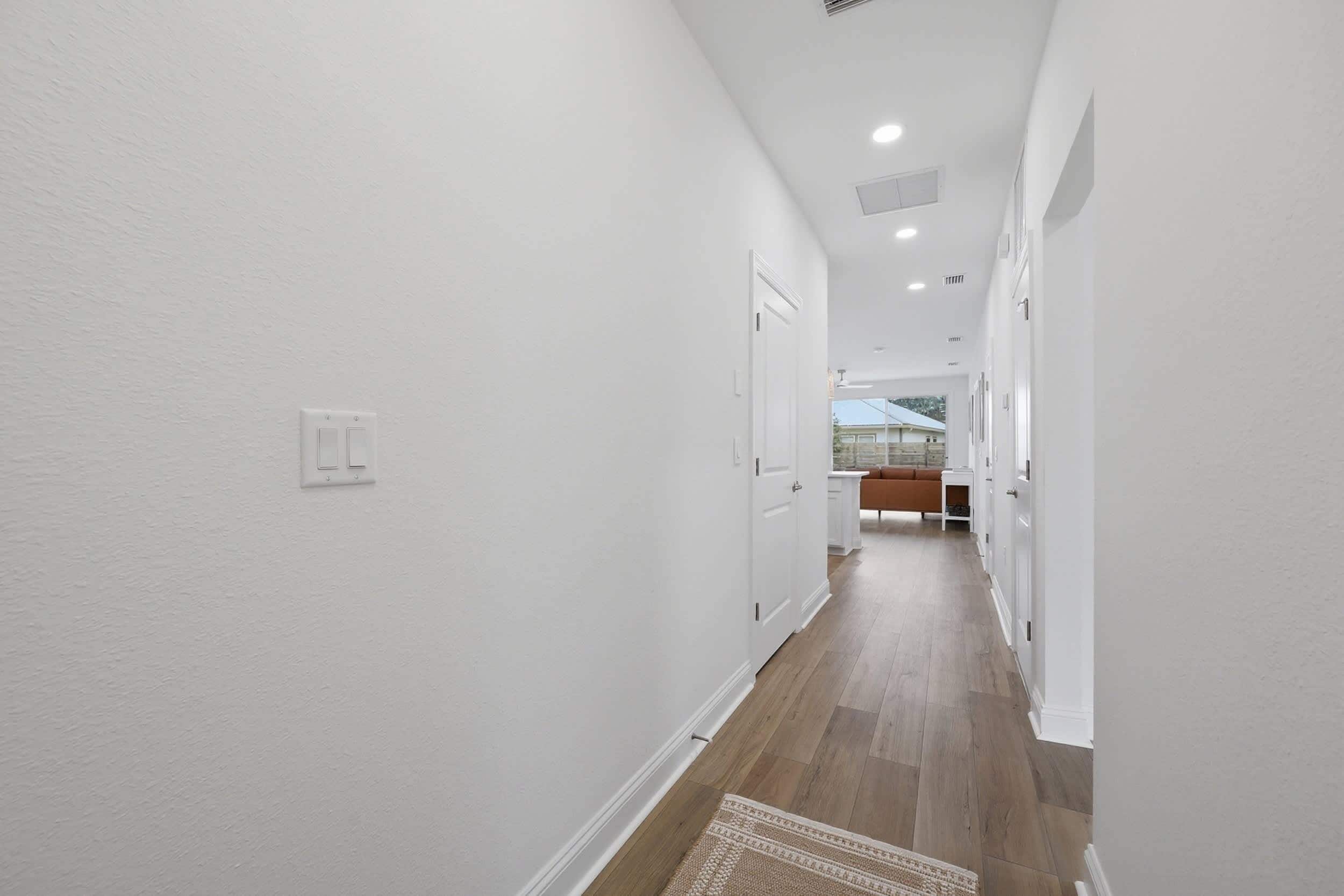 A hallway with white walls, wooden flooring, and recessed ceiling lights.