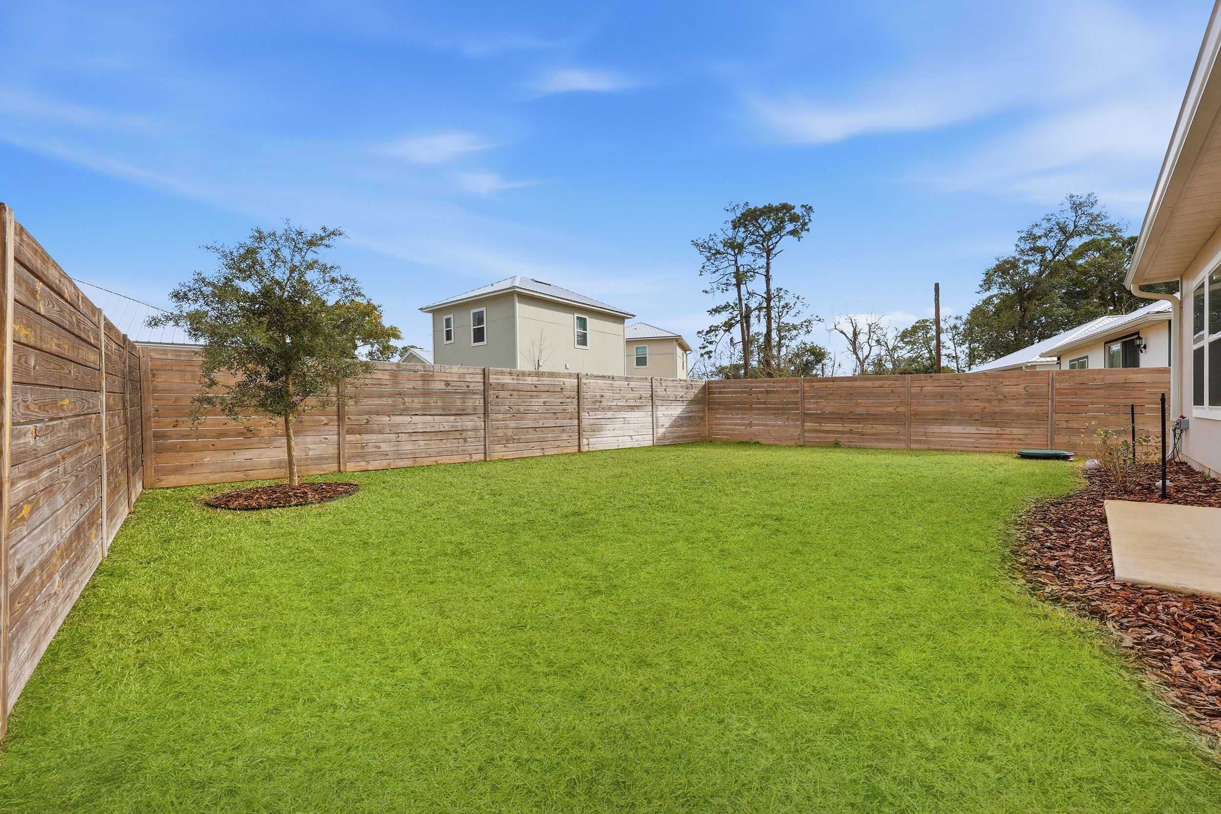 A backyard with a wooden fence, a small tree, and a house in the background.