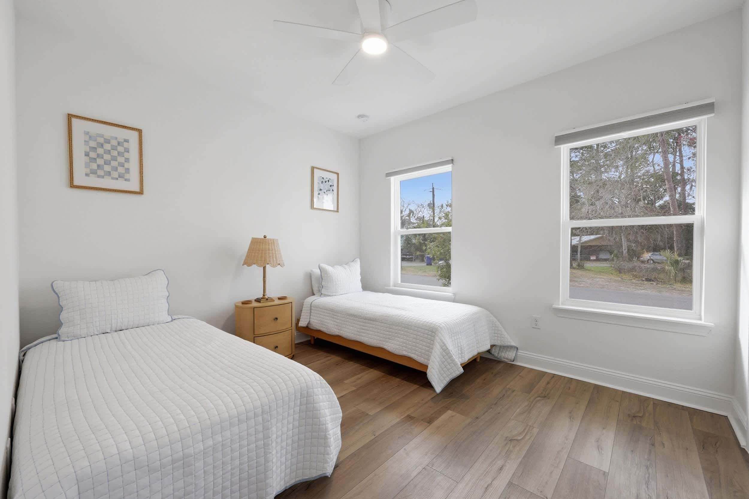 A bedroom with two beds, a ceiling fan, a window, and a nightstand.