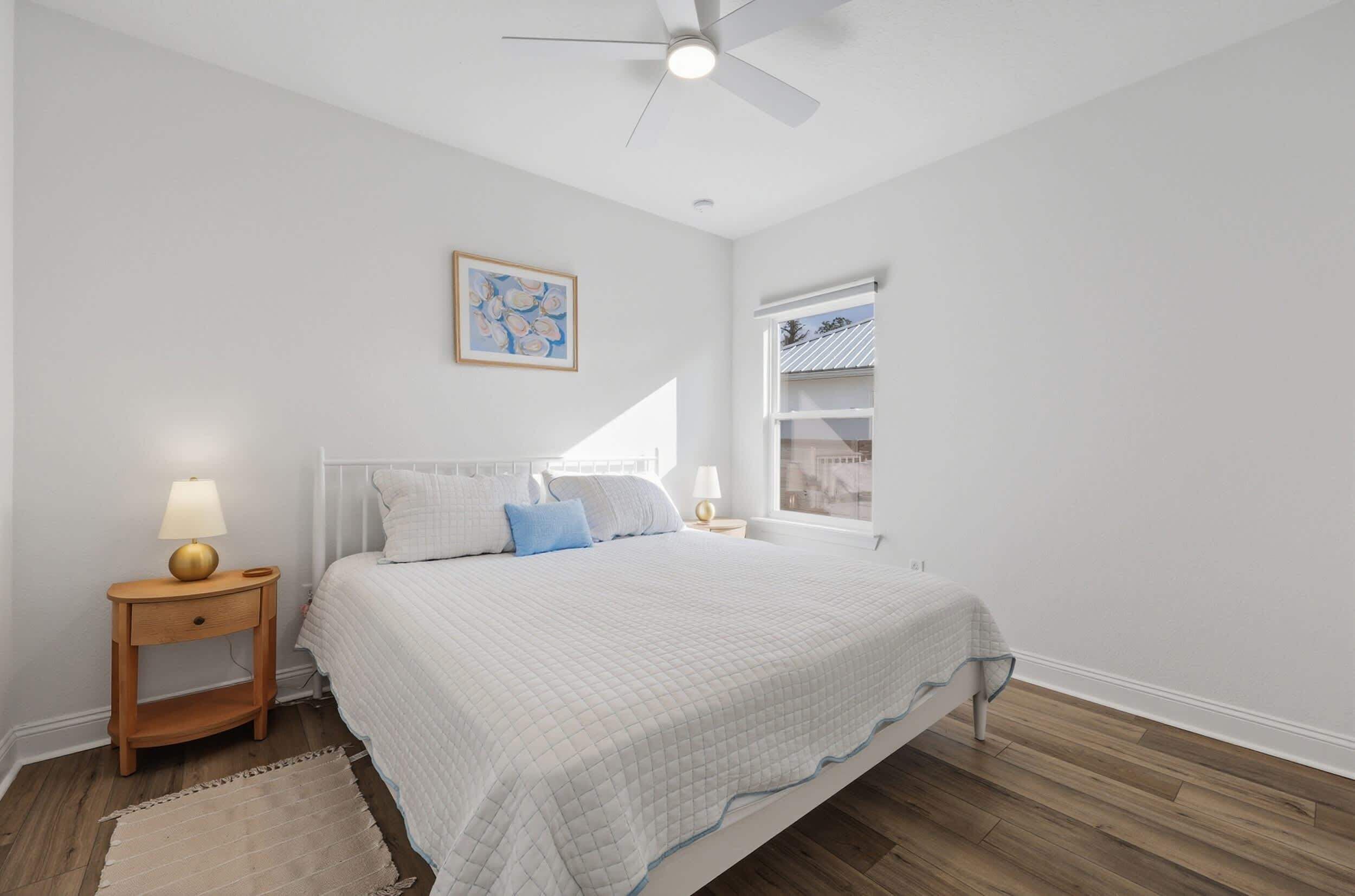 A bedroom with a bed, nightstand, lamp, and a ceiling fan.