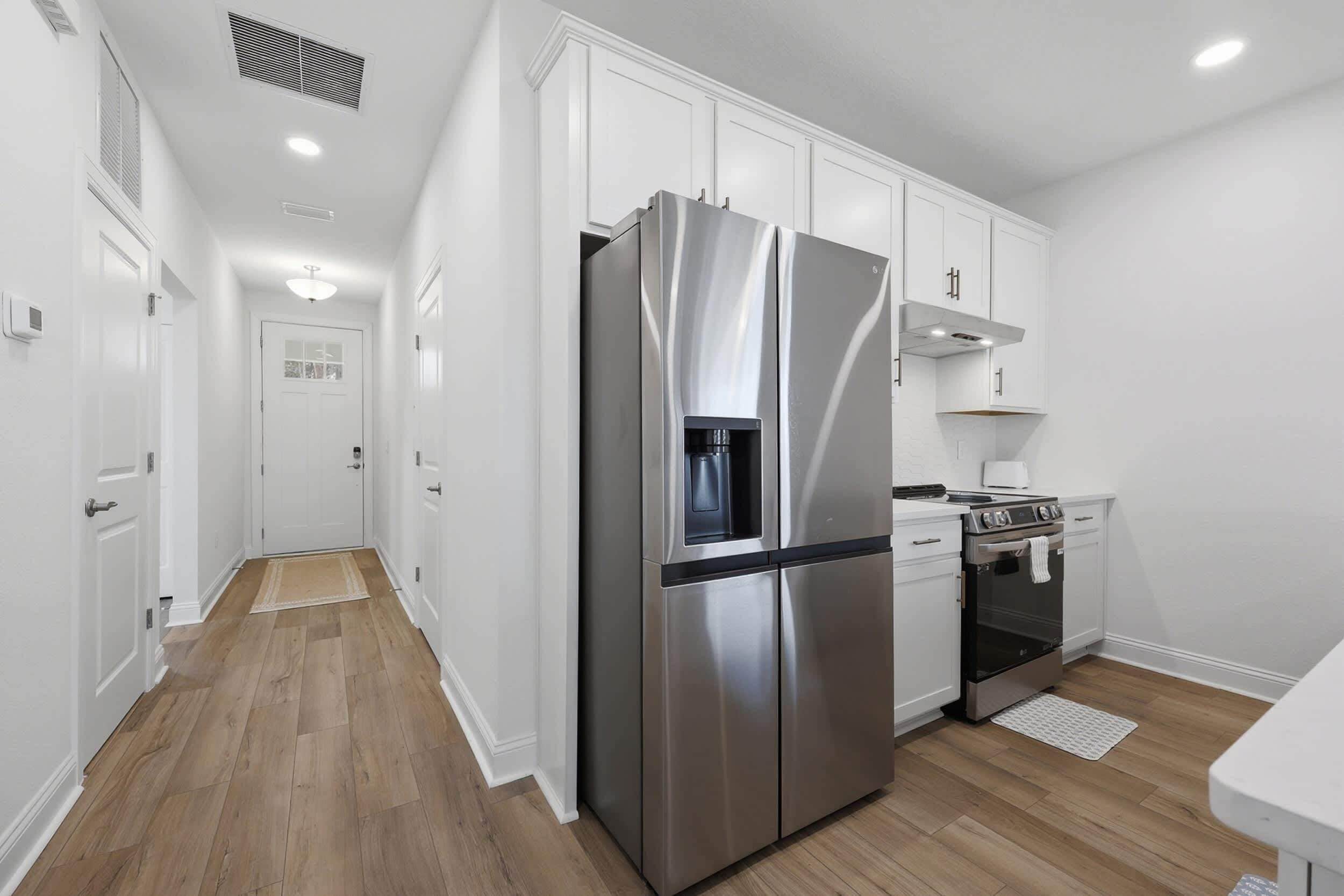 A modern kitchen with white cabinetry, a stainless steel refrigerator, a stove, and a microwave.