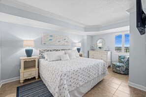 Ein Schlafzimmer mit Bett, Nachttischen, Kommode, Stuhl, Fenster und Bildern an der Wand.
