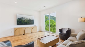 A modern living room with a wooden floor, a flat-screen TV mounted on the wall, a sofa, a coffee table, and a balcony with a view of greenery. - River Retreat 3307–Chattanooga Escape–Sleeps 13 (Chattanooga)