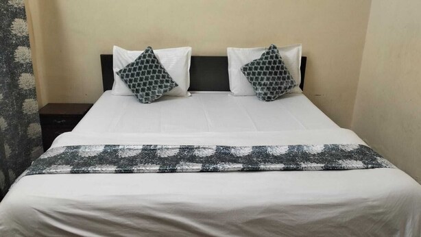 Ein Bett mit weißer Bettwäsche, zwei gemusterten Kissen, einem dunklen Kopfteil und einer grauen und weißen Tagesdecke.
