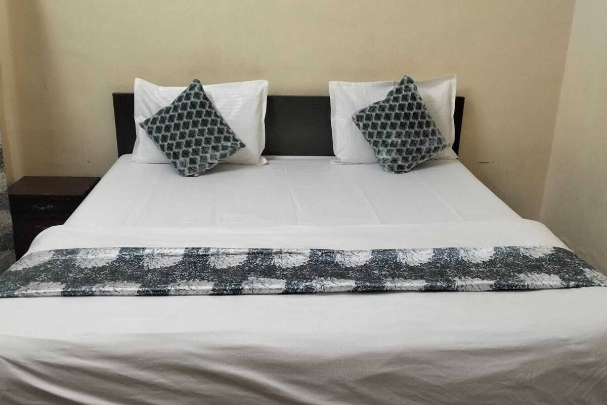 Una cama con ropa de cama blanca, dos almohadas estampadas, un cabecero oscuro y una manta estampada en gris y blanco.