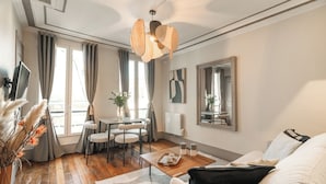 A modern living room with a sofa, a dining table with chairs, a TV, and a large mirror. - 1523 Verneuil (Paris)