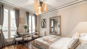 A hotel room with a bed, a desk, chairs, a large window, and a mirror. - 1523 Verneuil (Paris)