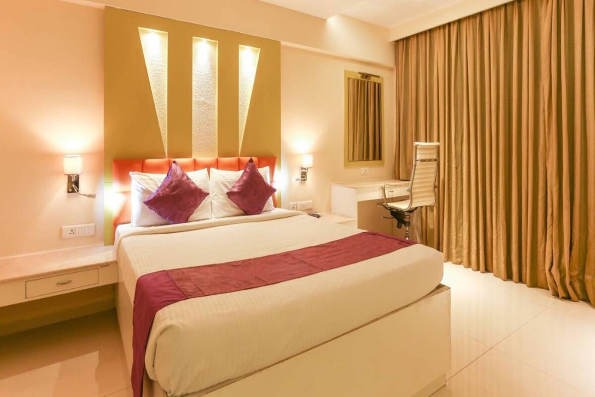 A hotel room with a bed, bedside table, lamp, curtains, and a mirror.
