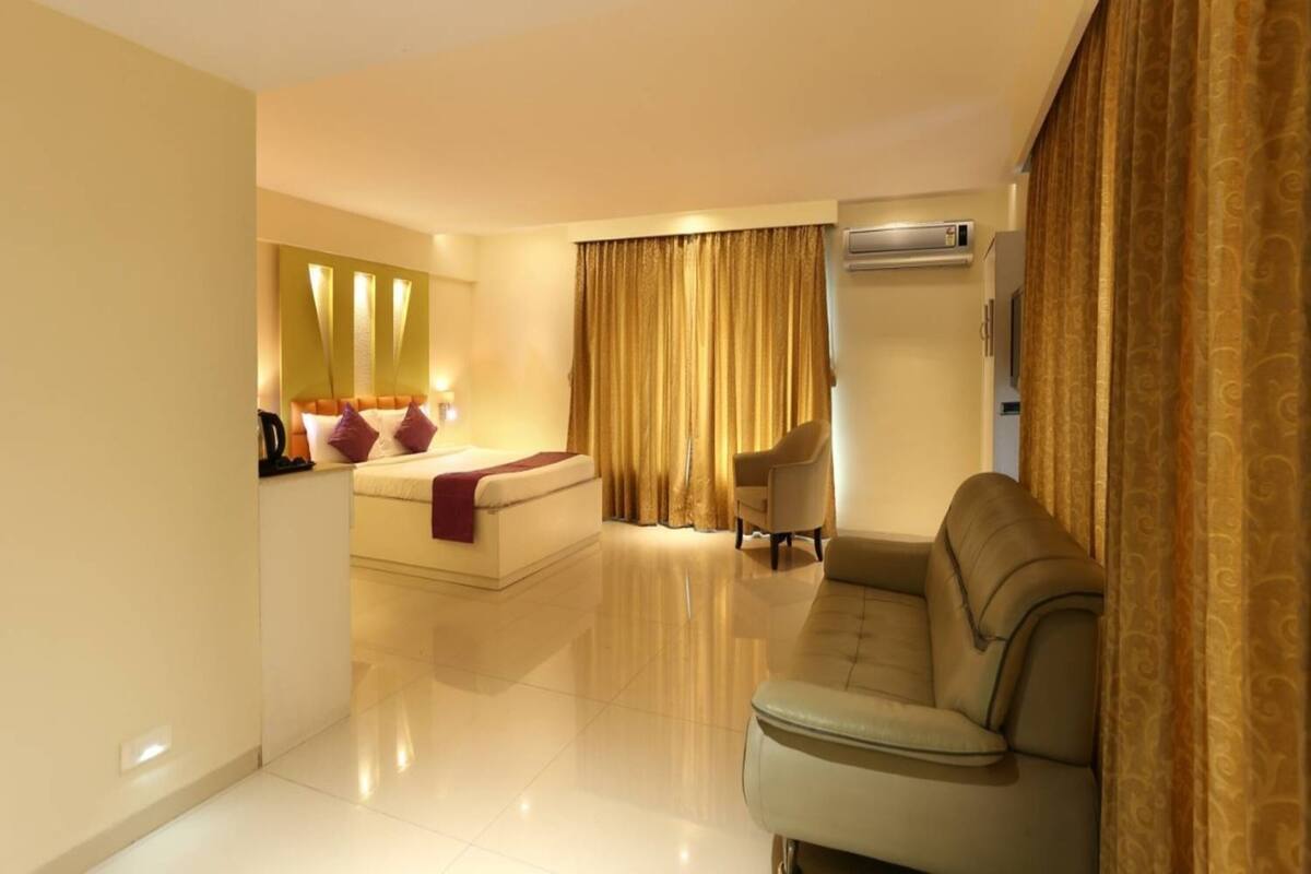 A hotel room with a bed, a sofa, a chair, a TV, and an air conditioning unit.