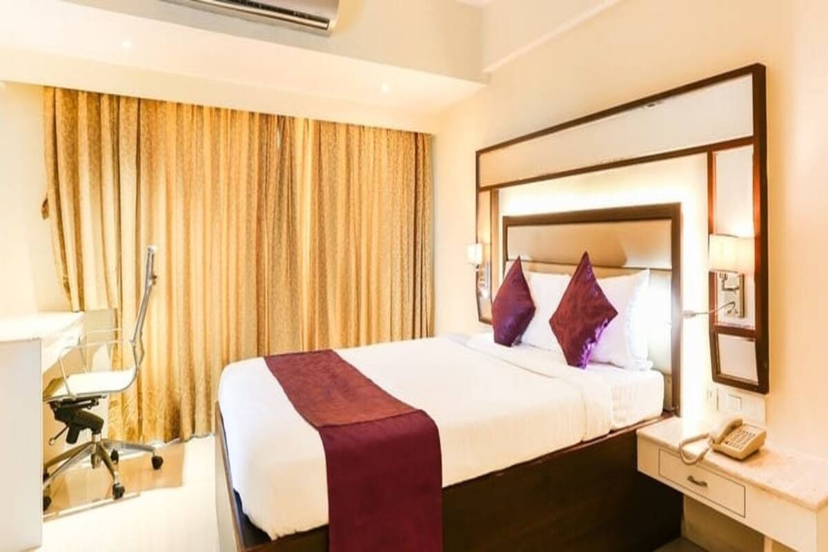 A hotel room with a bed, a desk, a chair, a telephone, and a curtain.